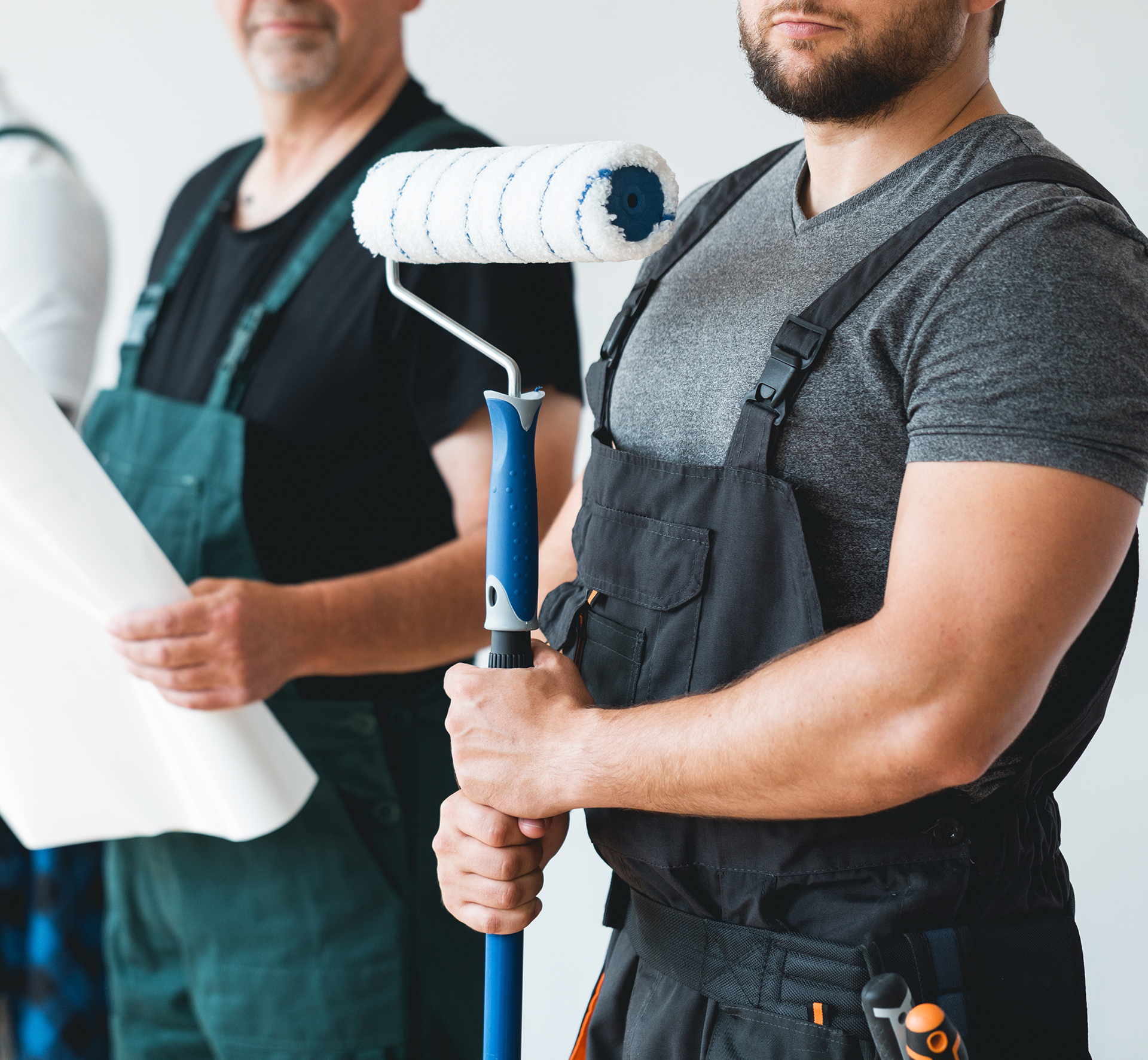 Close up of crew of three professional builder with painting roll and renovation plans standing in empty interior