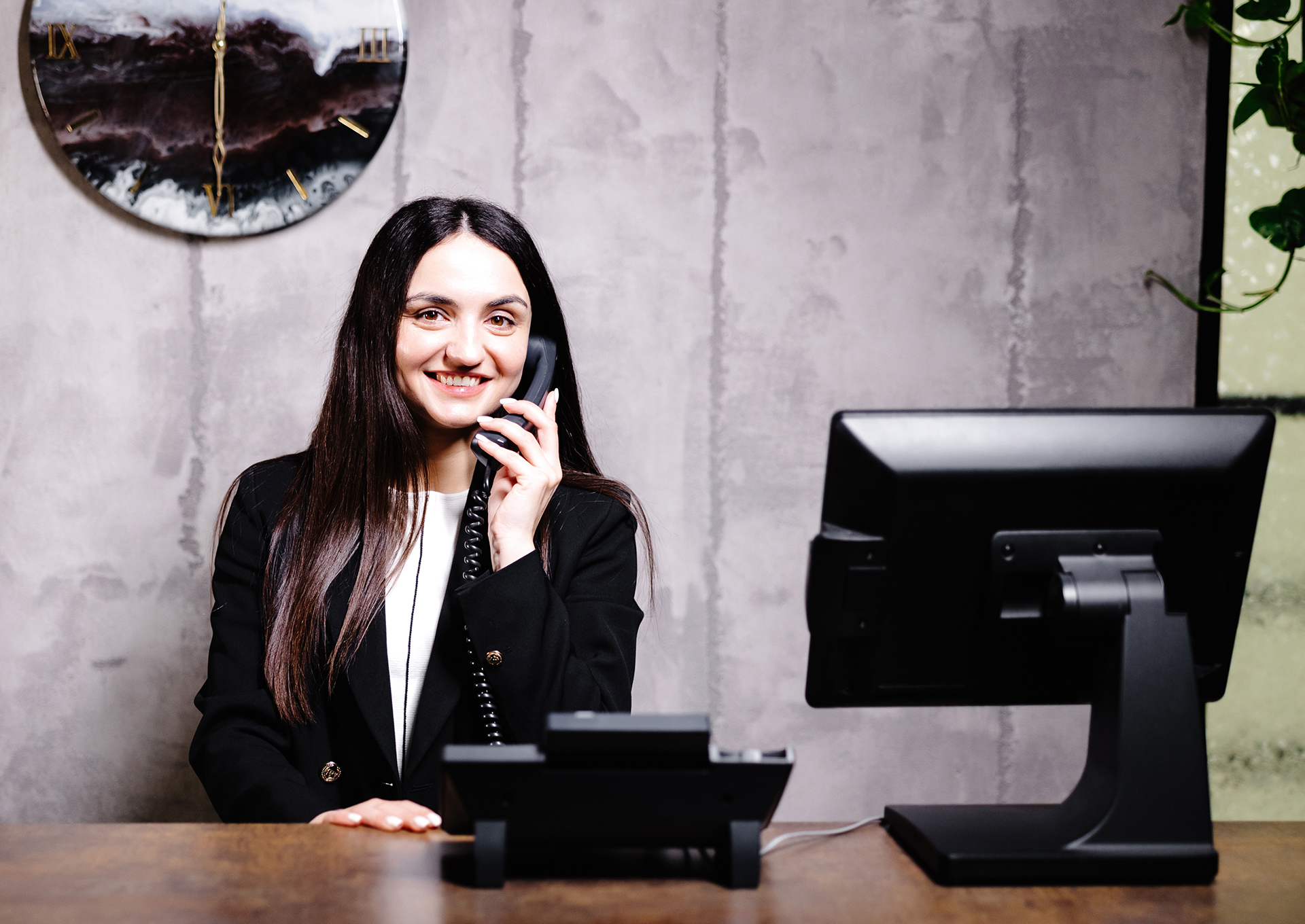 Hotel receptionist. Modern hotel reception desk with bell. Happy female receptionist worker standing at hotel counter and talking to phone